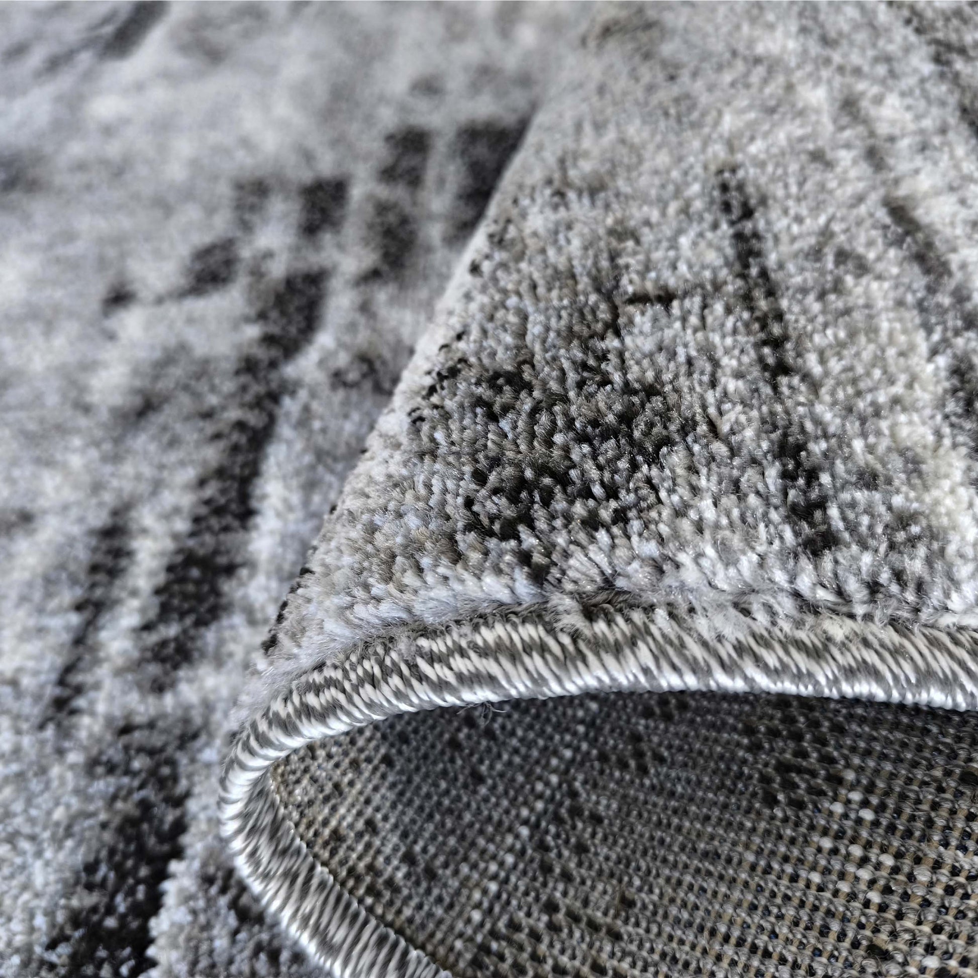 Gros plan d'un tapis aux nuances de gris et noir, présentant un motif abstrait et une texture épaisse et moelleuse, replié sur le côté