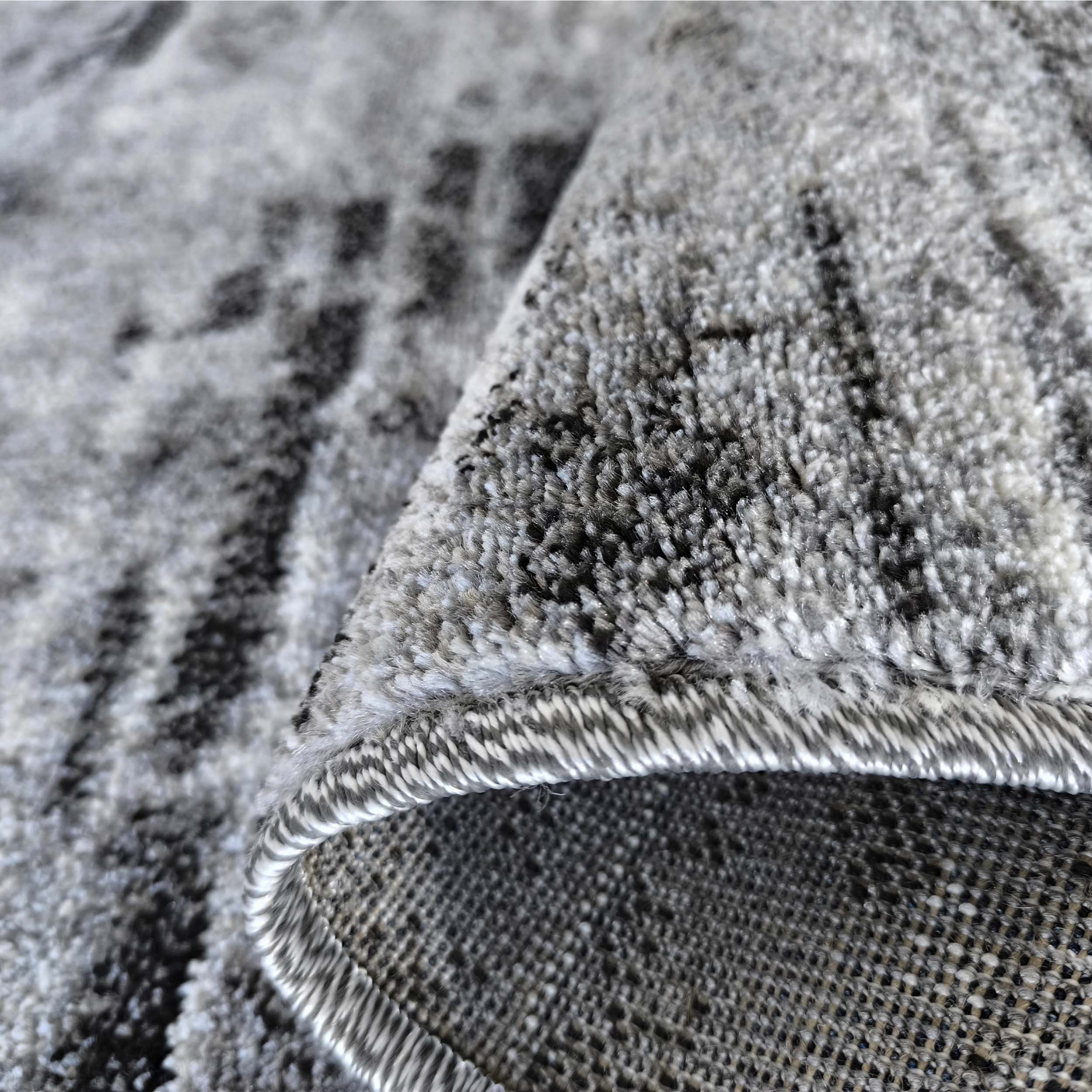 Gros plan d'un tapis aux nuances de gris et noir, présentant un motif abstrait et une texture épaisse et moelleuse, replié sur le côté