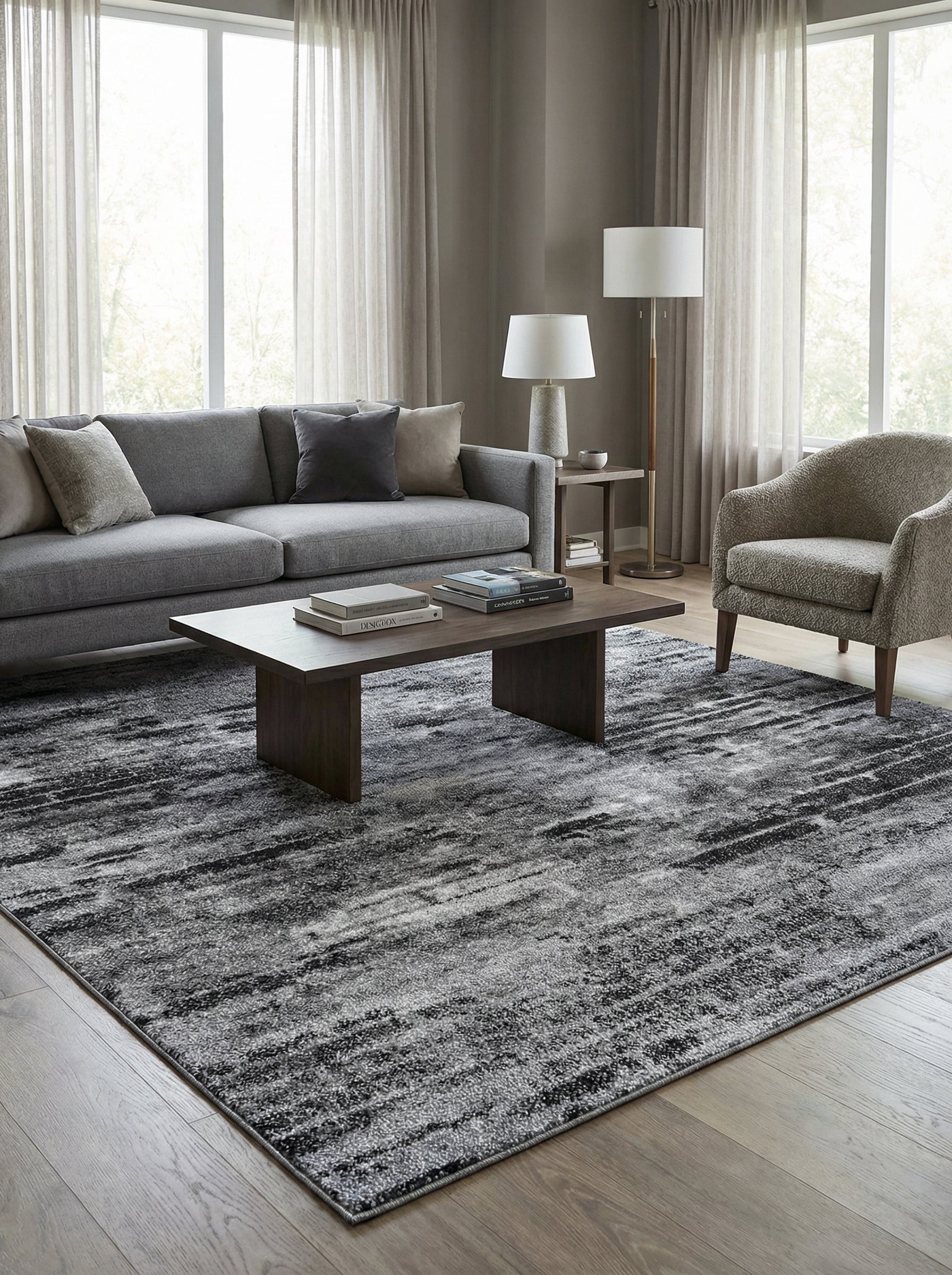 Grand tapis rectangulaire texturé aux nuances de gris clair, gris foncé et noir, avec un motif abstrait strié, dans un salon