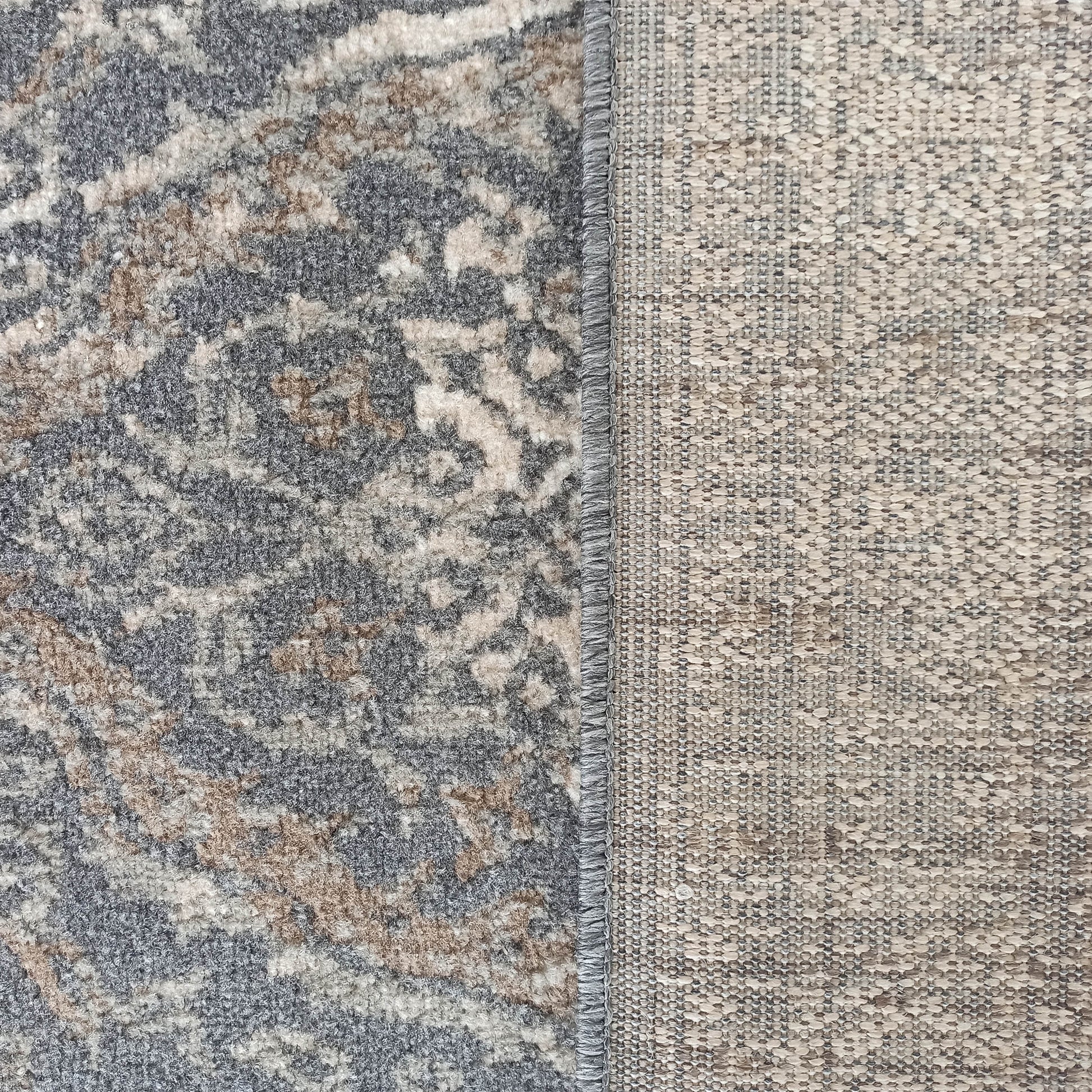 Gros plan sur un tapis montrant son côté pile texturé à motif abstrait gris, beige et blanc cassé, et son envers tissé clair