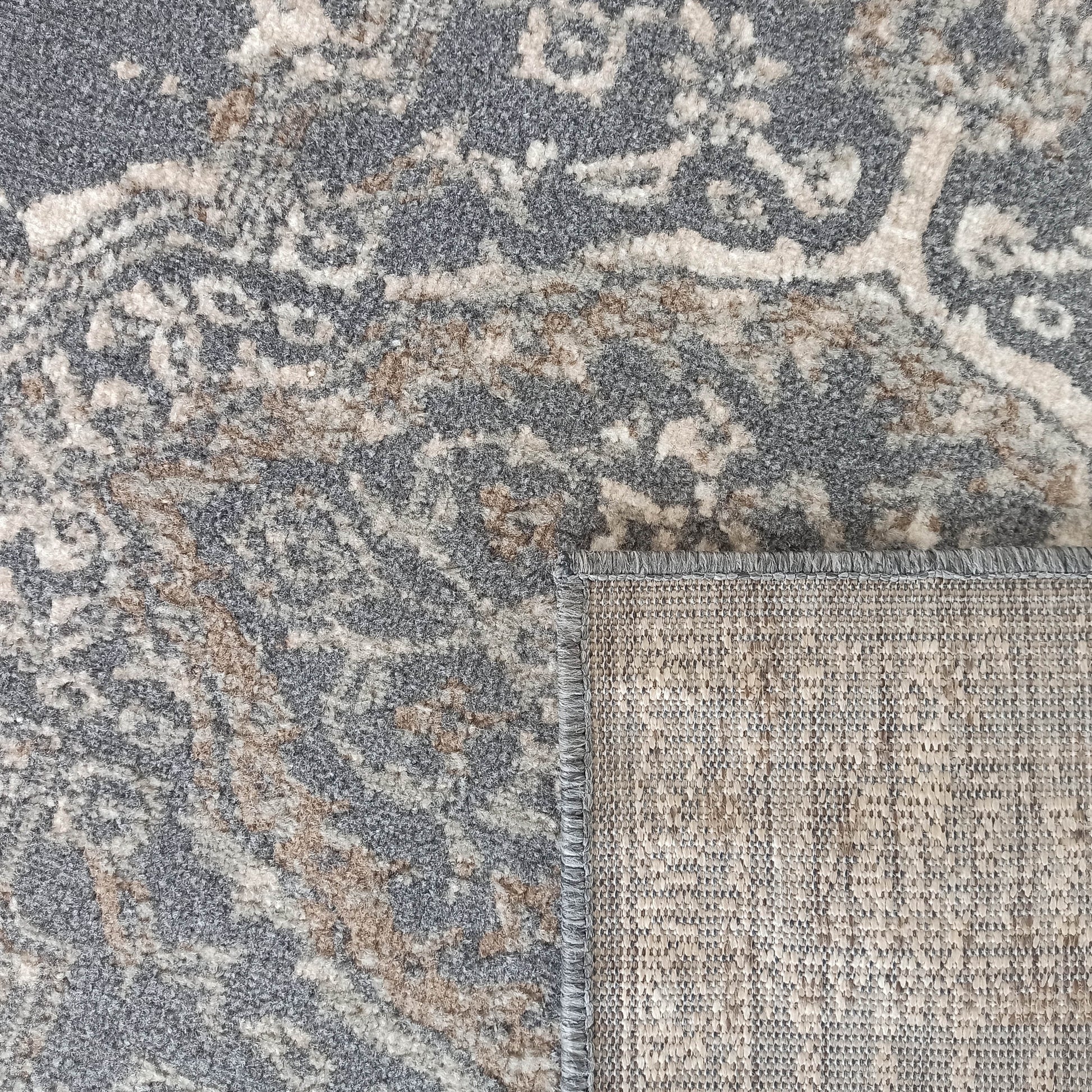 Tapis à motifs ornementaux gris foncé, beige clair et brun, avec une texture de poil douce et un revers tissé apparent