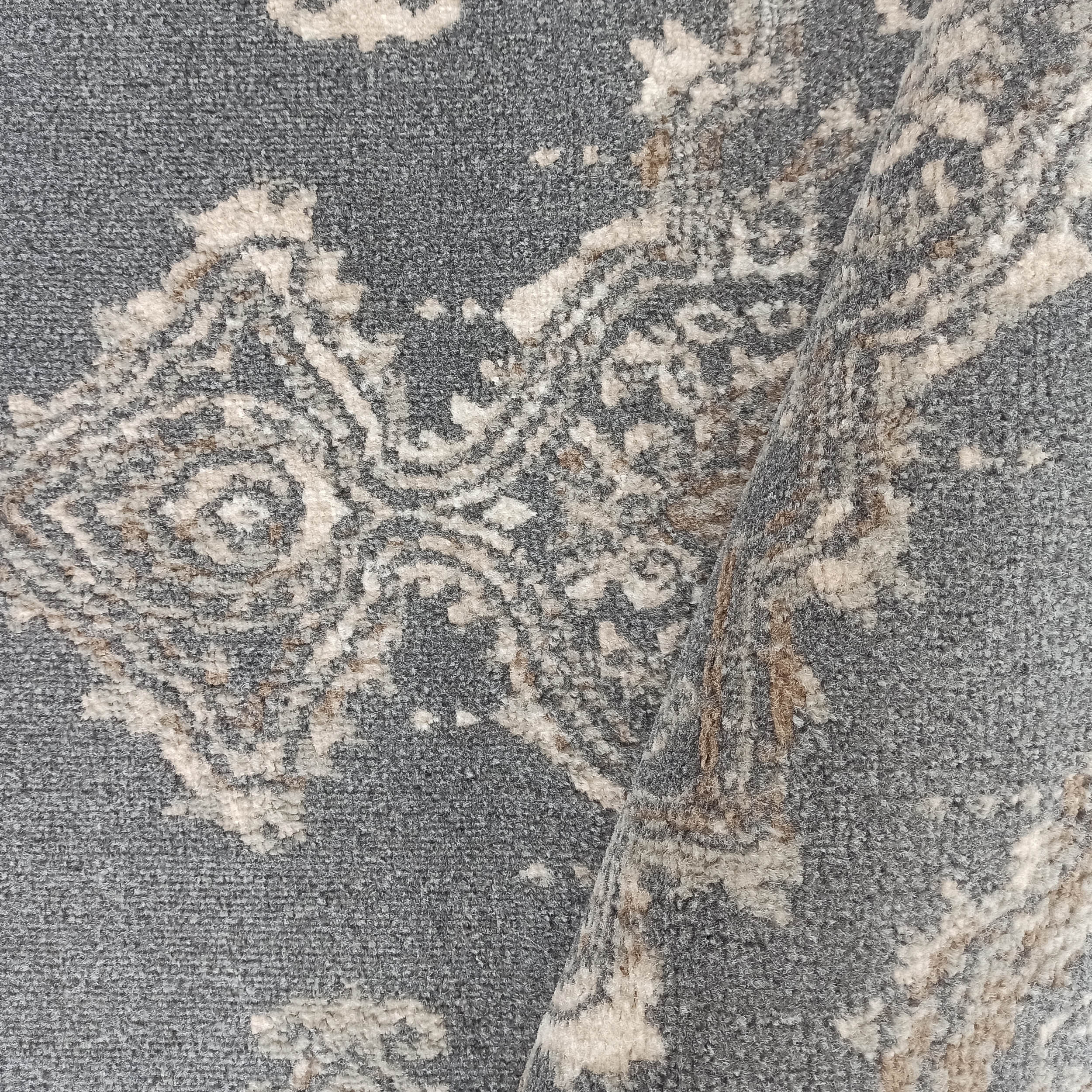 Tapis gris à poils longs orné de motifs abstraits beige crème et marron clair, une section est repliée