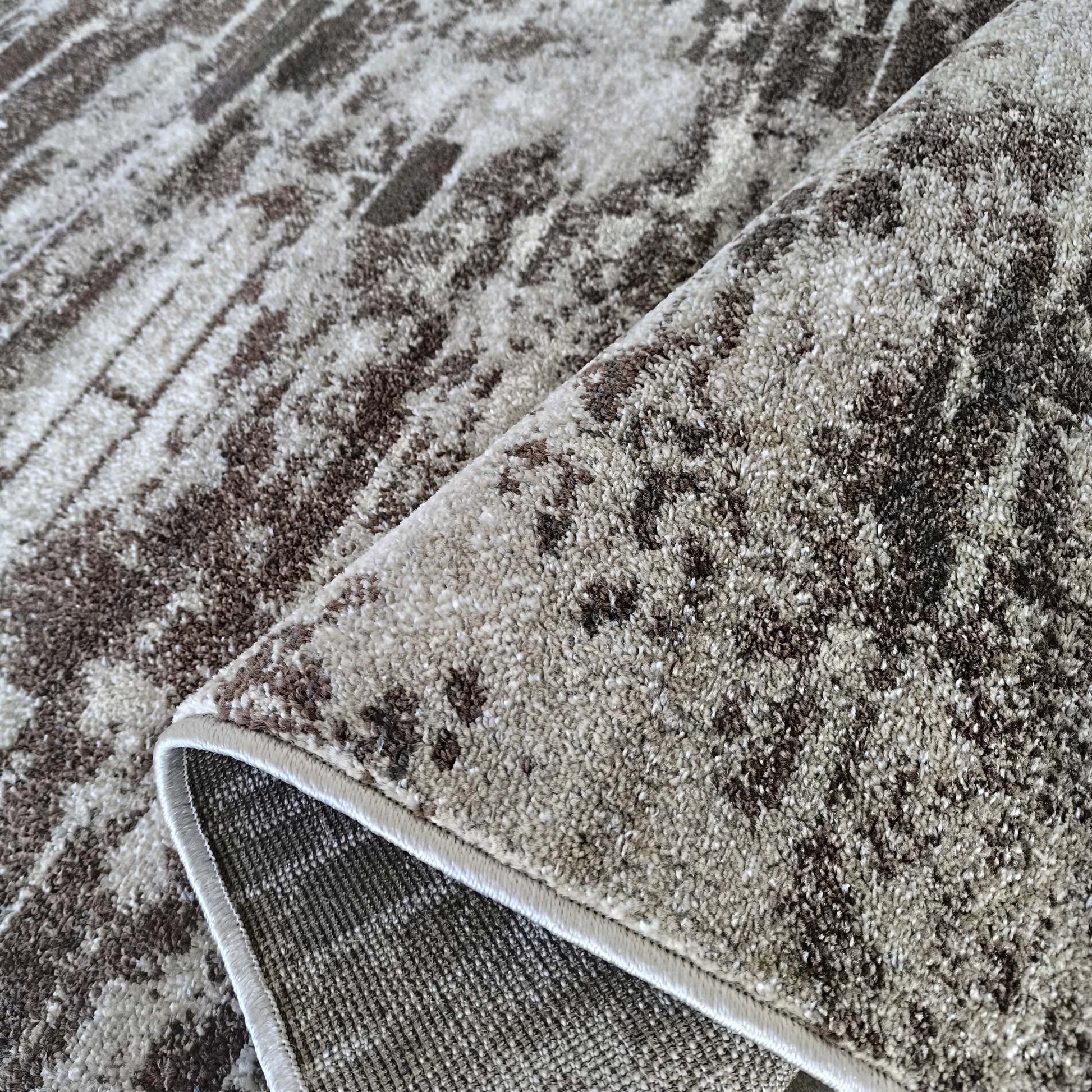 Tapis aux motifs abstraits marron et beige. Le tapis est plié, montrant sa texture douce et son revers tissé