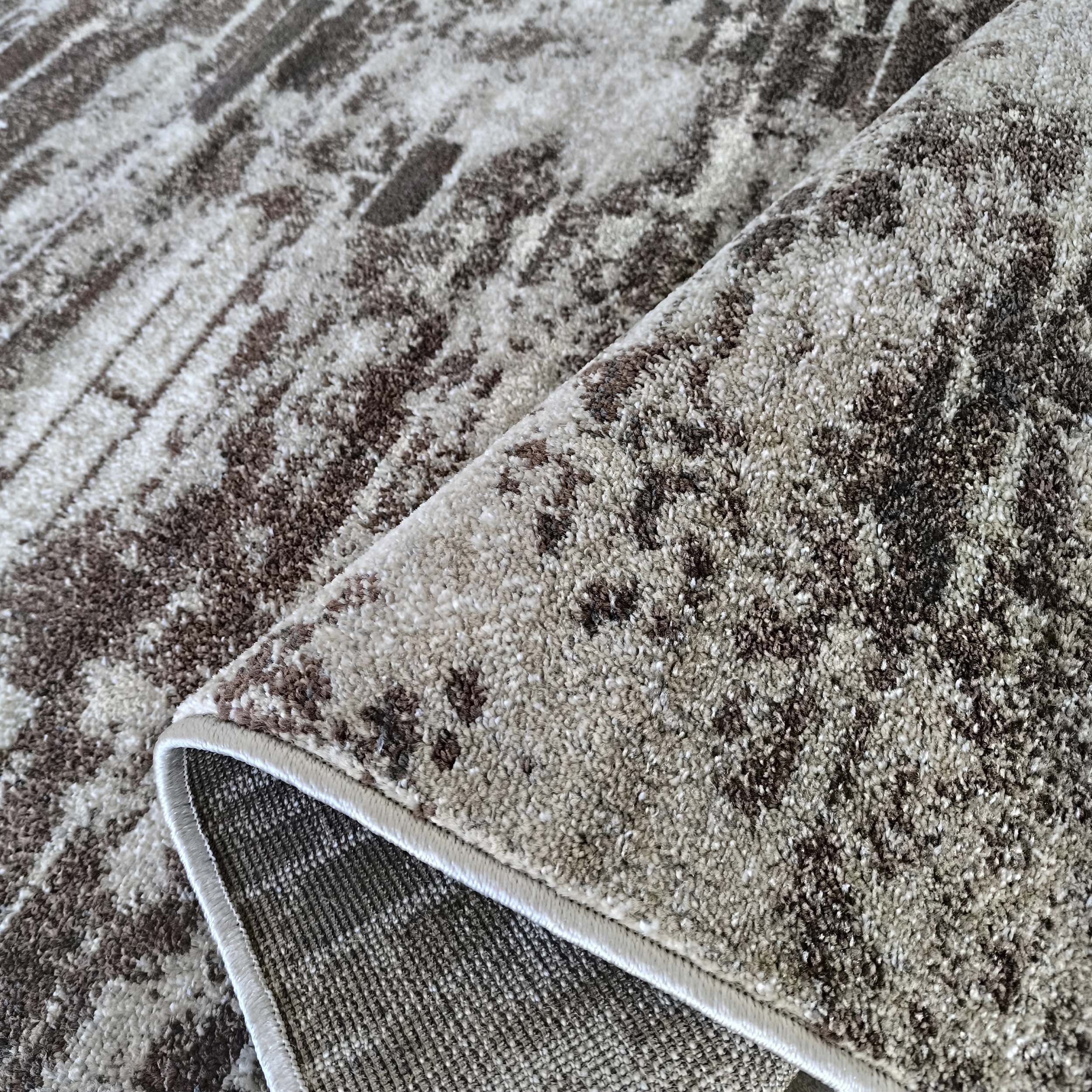 Tapis aux motifs abstraits marron et beige. Le tapis est plié, montrant sa texture douce et son revers tissé