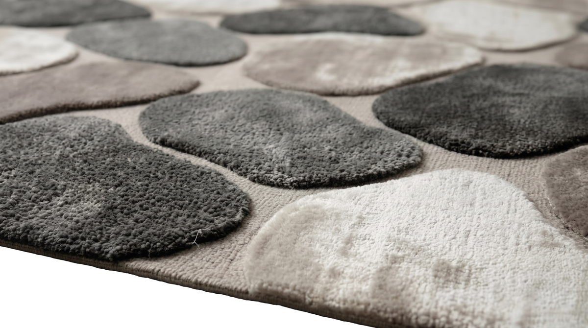 La laine et la viscose forment un relief texturé de galets gris et taupe, soulignant l'épaisseur du tapis